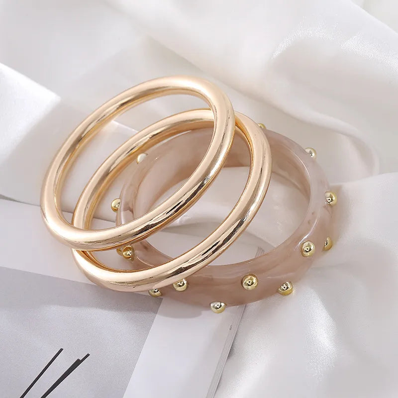 Set of three bangles: two polished gold-tone and one blush resin with gold studs