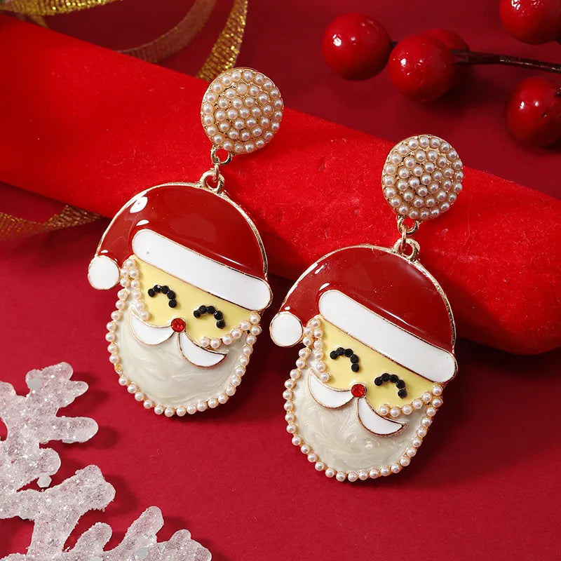 Santa Claus face drop earrings with pearl-studded top and beard, featuring red hat and festive enamel detailing on a red background.