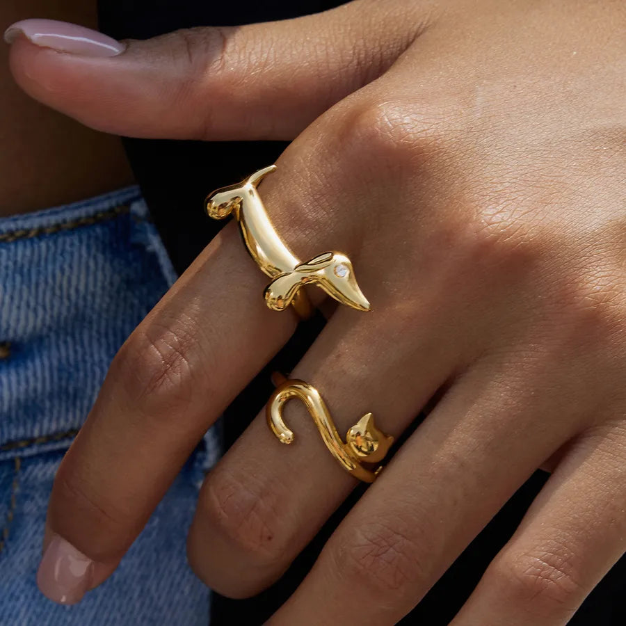Close-up of two gold adjustable rings shaped like a cat and a dog, from The Layers jewellery collection.