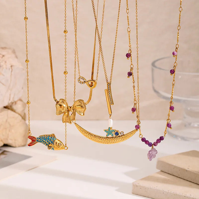Set of gold-plated charm necklaces featuring moon, bow, gemstone, and enamel fish pendants — elegant handcrafted jewelry from The Layers.