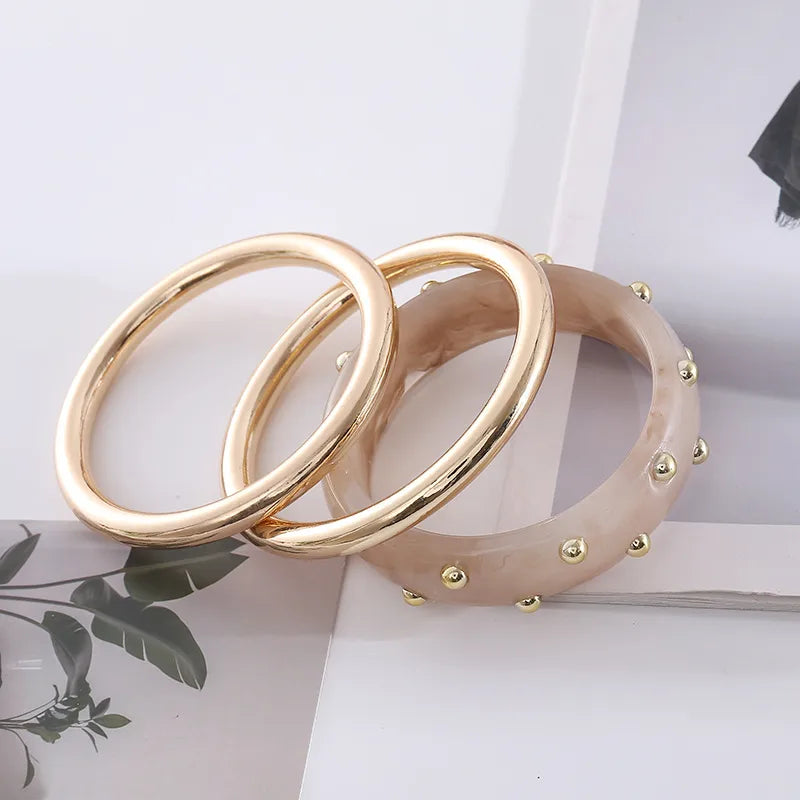 Gold-tone stacking bangles with blush resin studded bangle — set of 3 on neutral background
